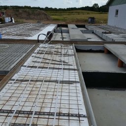 Damian Jabłonowski - Fundamenty domu jednorodzinnego w trakcie budowy: zbrojenie, izolacja termiczna i instalacja ogrzewania podłogowego. Widok z góry na plac budowy.