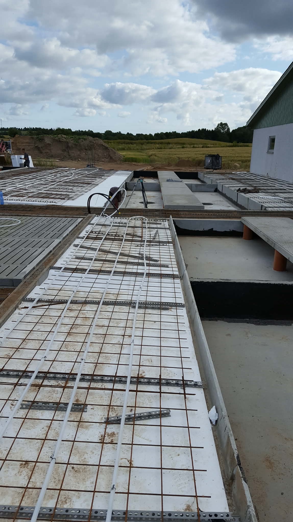 Fundamenty domu jednorodzinnego w trakcie budowy: zbrojenie, izolacja termiczna i instalacja ogrzewania podłogowego. Widok z góry na plac budowy.