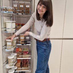 Sommer House Ewa Sommerfeld - Uśmiechnięta kobieta prezentuje wysuwaną spiżarnię z zapasami żywności w pojemnikach. Porządek i organizacja w kuchni.