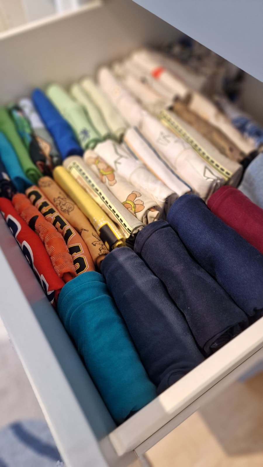 Uporządkowana szuflada z kolorowymi ubraniami zwiniętymi w rulony, widok z góry. Organizacja przestrzeni w szafie, Warszawa.