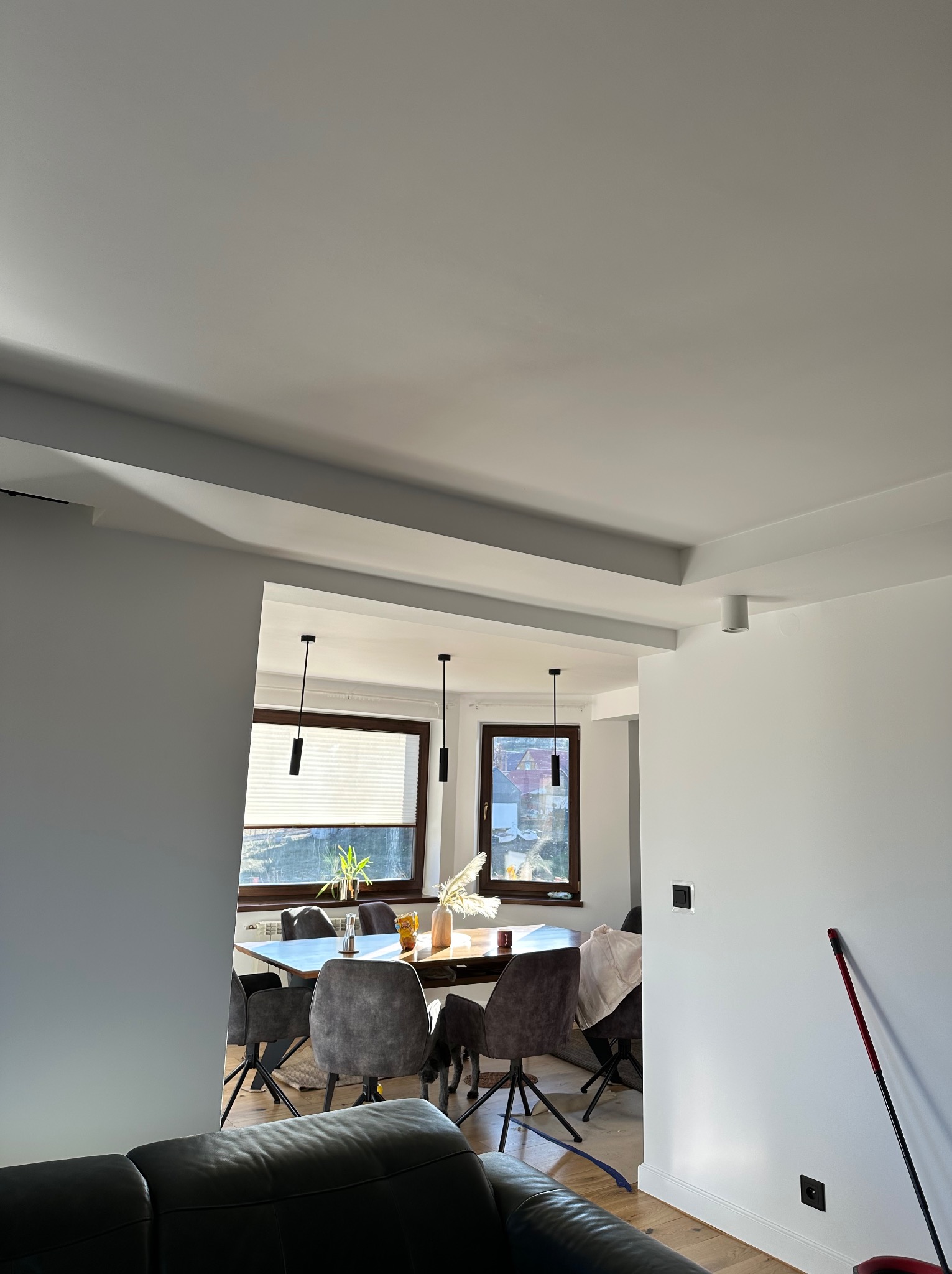 Jasne, nowocześnie wykończone wnętrze z widokiem na jadalnię. Ściany pomalowane na biało, widoczne detale architektoniczne i minimalistyczne oświetlenie.