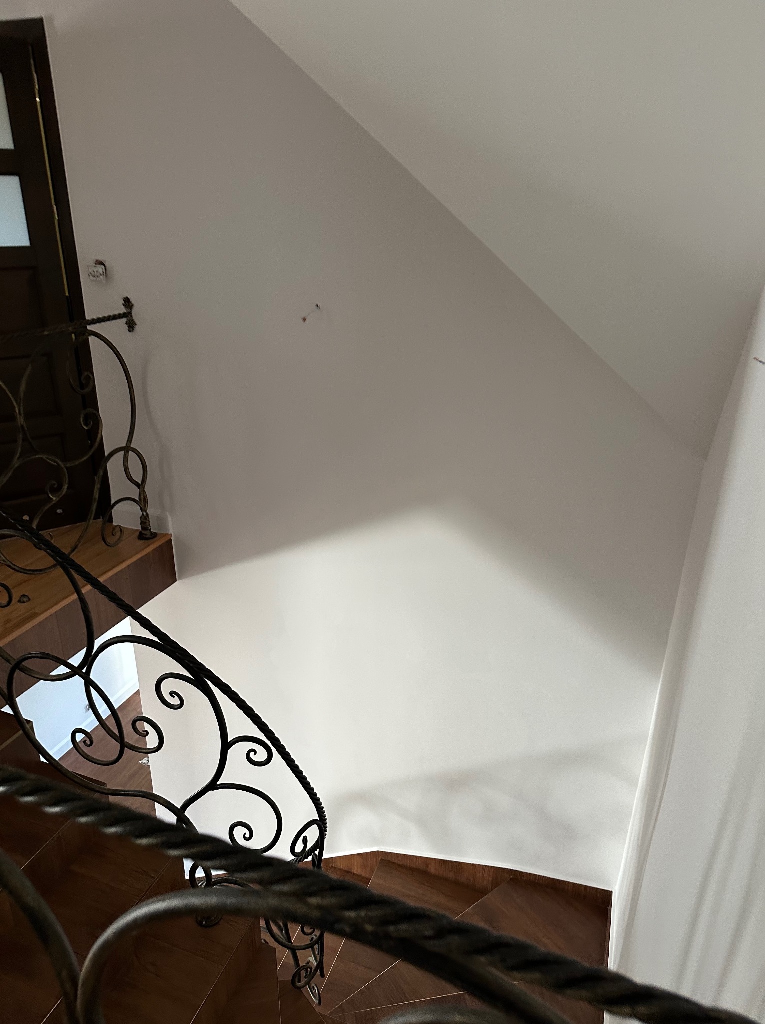 Ściana po świeżym odnowieniu, widoczna z góry, z fragmentem ozdobnej, metalowej balustrady schodów i drewnianymi stopniami. Minimalistyczny design.