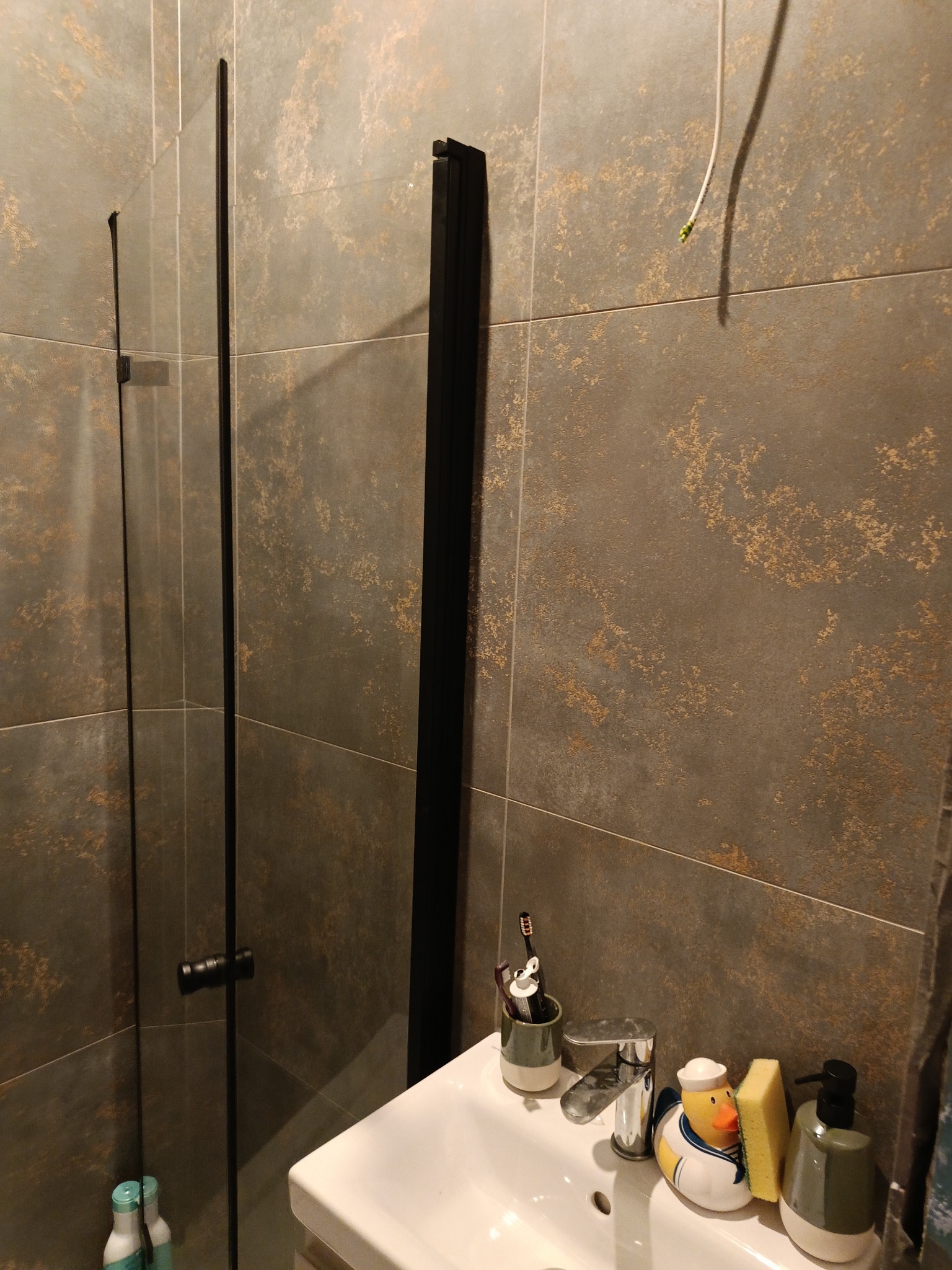 Nowoczesna łazienka z kabiną prysznicową typu walk-in, wykończona płytkami imitującymi metal. Umywalka z baterią i akcesoriami.