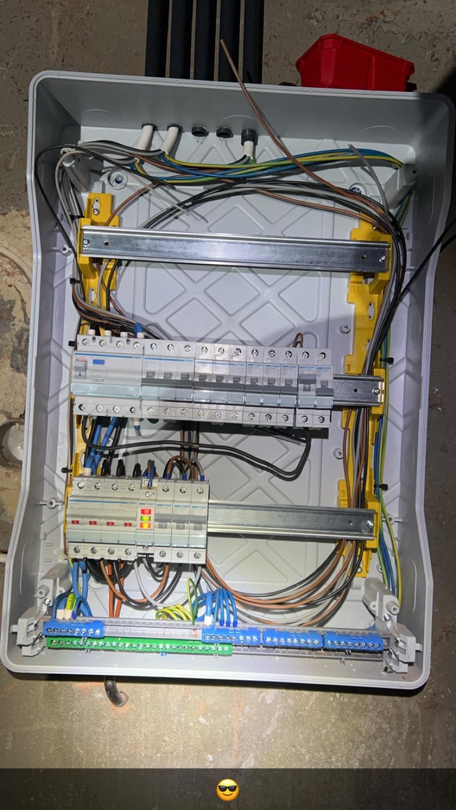 Rozdzielnica elektryczna w trakcie montażu, widoczne kable, bezpieczniki i listwy zaciskowe w szarej obudowie. Ujęcie z góry, widoczne elementy instalacji.