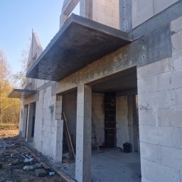 Szymon Stalke - Surowy stan domu z betonu komórkowego w trakcie budowy, widoczne stropy i ściany, na zewnątrz drzewa z jesiennymi liśćmi, ziemia częściowo błotnista.