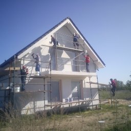 PIOTR DOMAŃSKI - Ekipa na rusztowaniu podczas prac elewacyjnych w Myśliborzu. Widoczny dom jednorodzinny w trakcie malowania, narzędzia i materiały budowlane.