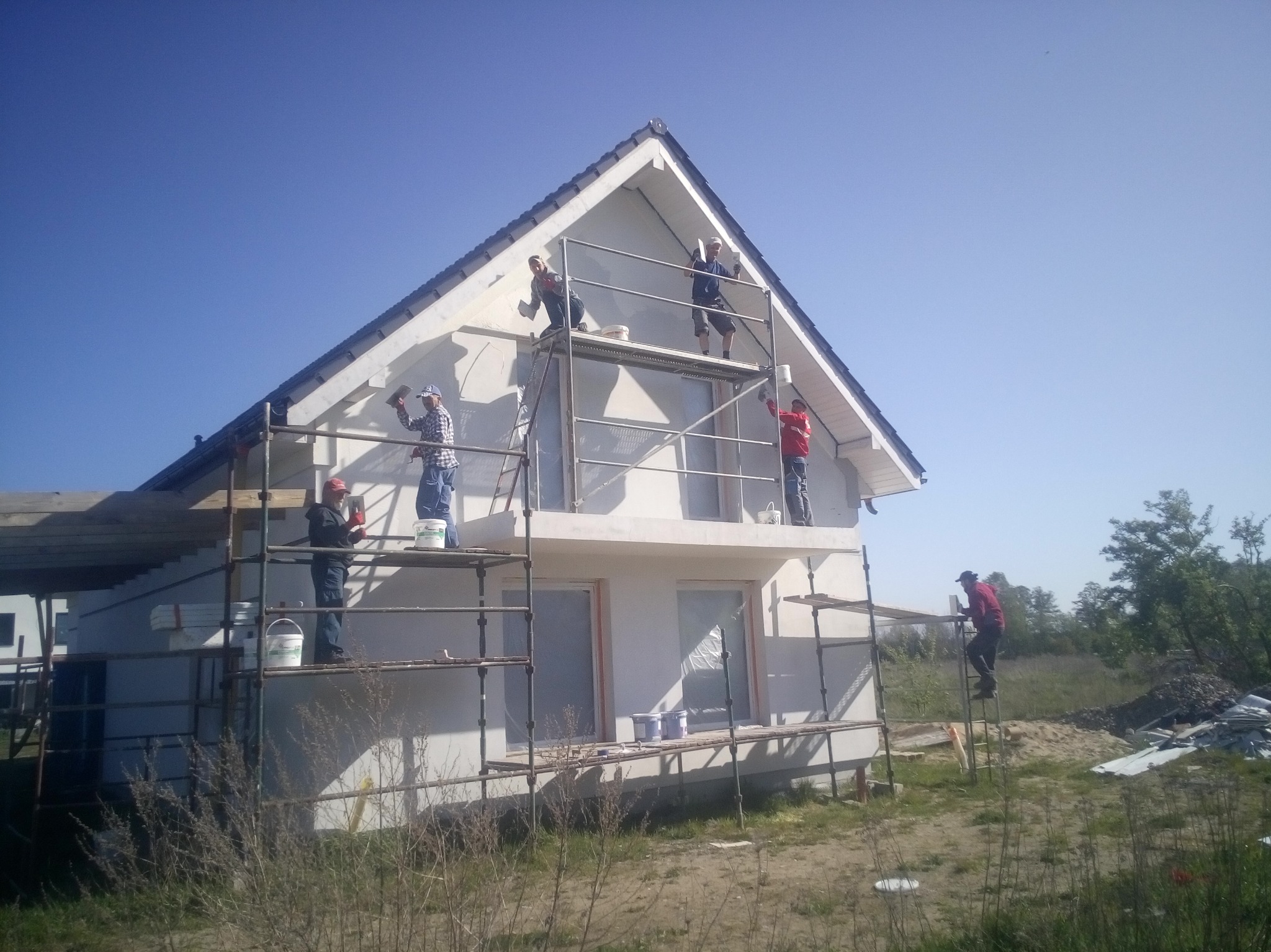 Ekipa na rusztowaniu podczas prac elewacyjnych w Myśliborzu. Widoczny dom jednorodzinny w trakcie malowania, narzędzia i materiały budowlane.