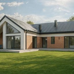 Sylwia Rybacka Architekt&Projektowanie Wnętrz - Parterowy dom z dachem dwuspadowym, wykończony cegłą i białym tynkiem, z dużymi oknami i tarasem. Widok z ogrodu, w tle drzewa i błękitne niebo.