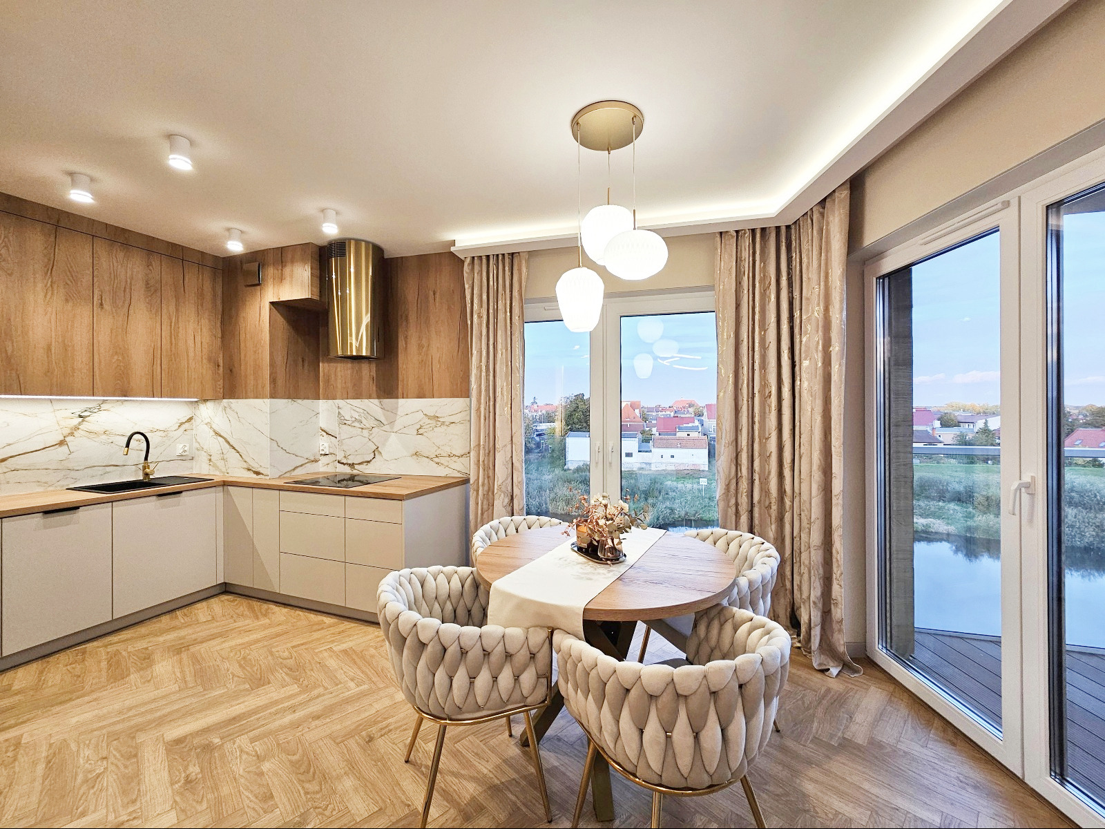 Jasna kuchnia z drewnianymi akcentami i marmurowym backsplashiem. Okrągły stół z krzesłami w stylu glamour przy oknie z widokiem na jezioro.