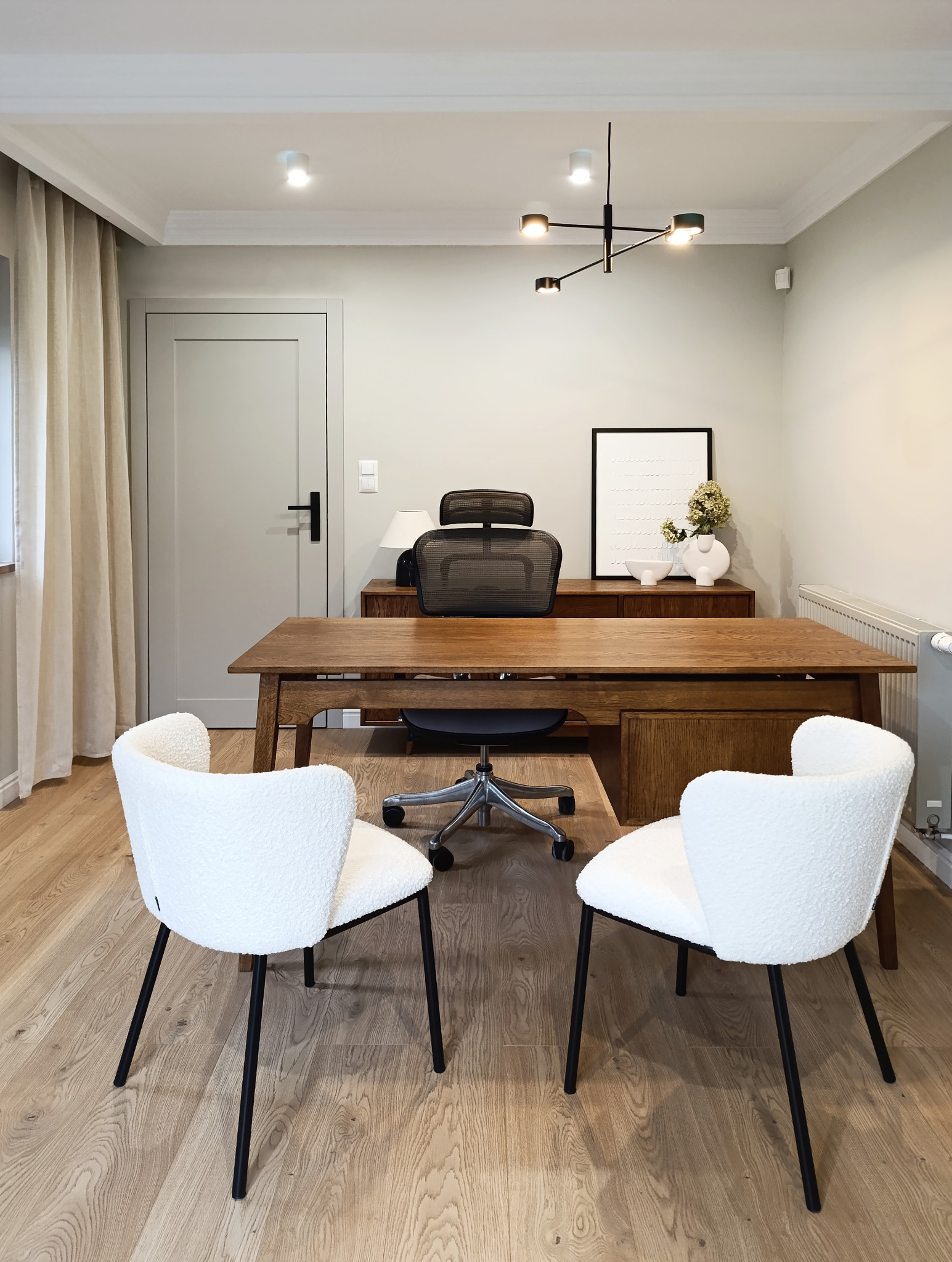 Nowoczesne biuro domowe z drewnianym biurkiem, krzesłem biurowym i dwoma białymi krzesłami. Minimalistyczny wystrój, lampa sufitowa i drewniana podłoga.