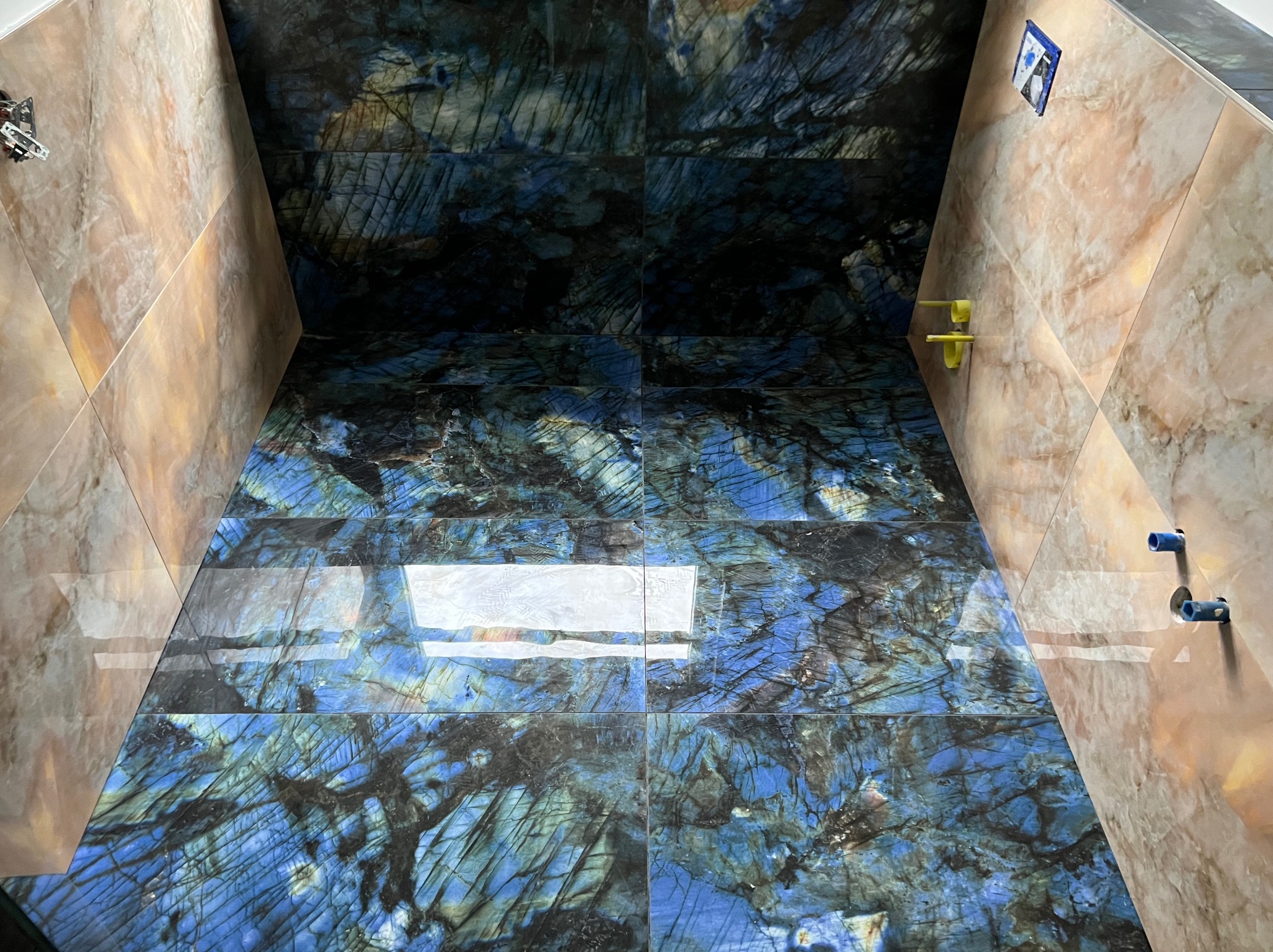 Wykończona łazienka z marmurowymi płytkami w odcieniach niebieskiego i brązowego, z widocznymi elementami instalacji wodnej i elektrycznej. Nietypowy wzór płytek.