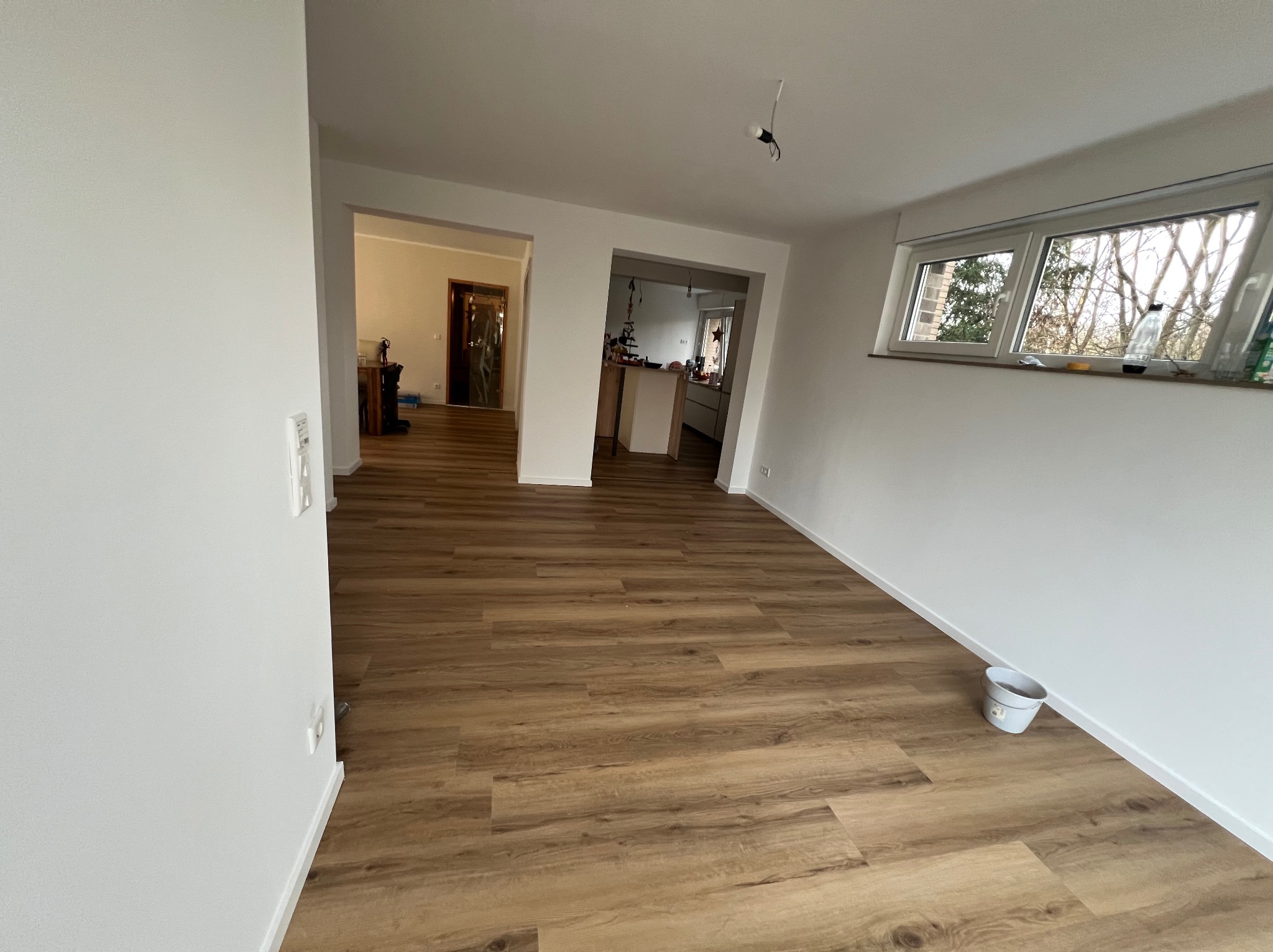 Jasne wnętrze po remoncie: świeżo pomalowane ściany, ułożona podłoga z paneli imitujących drewno. Widok na sąsiednie pomieszczenia przez otwarte przejścia.