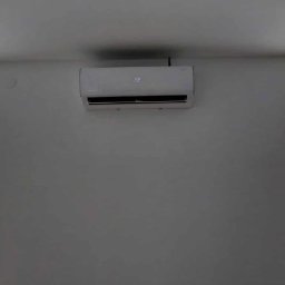 IzoKlima Zbigniew Jarmuziak - Biały klimatyzator ścienny z wyświetlaczem temperatury 22 stopnie, zamontowany w jasnym pomieszczeniu z dwoma oknami z żaluzjami poziomymi.