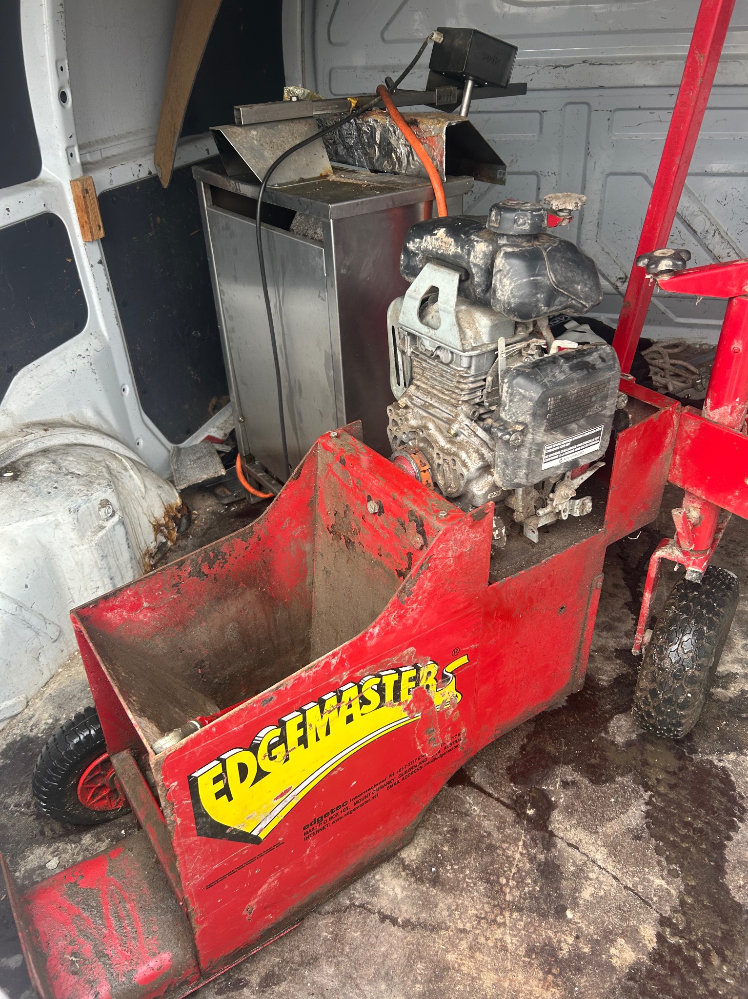 Czerwona, używana krawędziarka do trawników 'Edgemaster' z silnikiem spalinowym, stojąca wewnątrz furgonetki. Widoczne ślady użytkowania i zabrudzenia.