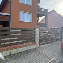 DK spawanie & Budownictwo - Drewniane ogrodzenie poziome z kamiennymi słupkami i elementami z cegły klinkierowej, przylegające do domu z brązową elewacją. Pies wygląda zza ogrodzenia.