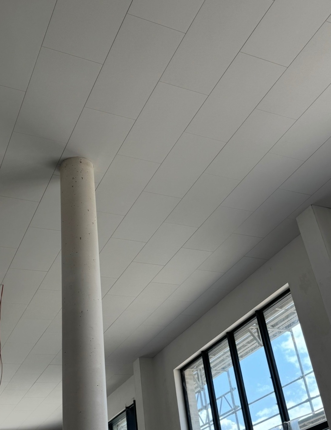 Biały sufit kasetonowy z kolumną w nowoczesnym wnętrzu, widok z dołu. Okno z widokiem na niebo. Realizacja z Bydgoszczy.
