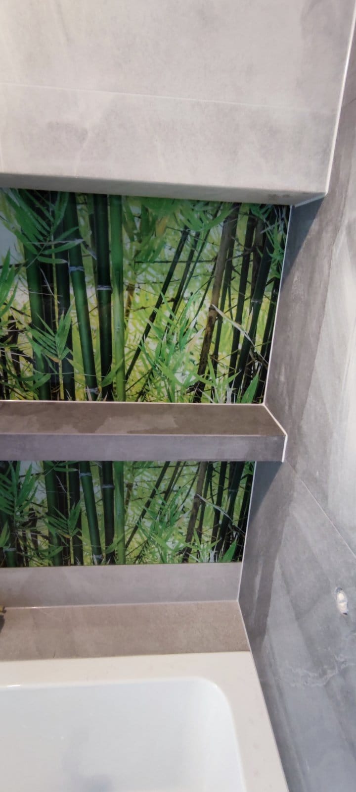 Wykończona ściana w łazience z motywem bambusa, szare płytki, półki. Widoczny fragment wanny. Ujęcie z dołu, podkreślające detale wykończenia.