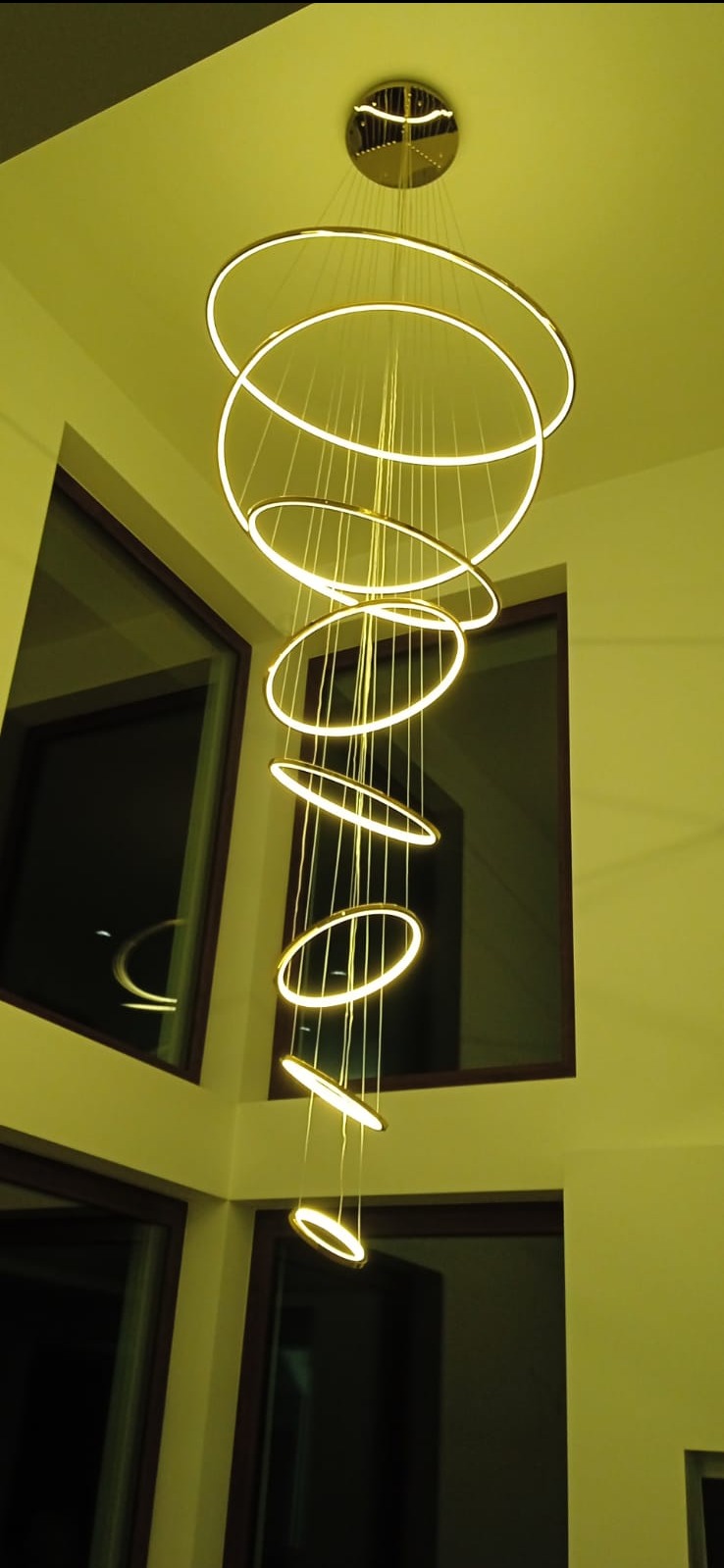 Nowoczesny żyrandol LED z okrągłymi elementami zawieszony w przestronnym wnętrzu z oknami. Ciepłe światło podkreśla minimalistyczny design i tworzy przytulną atmosferę.