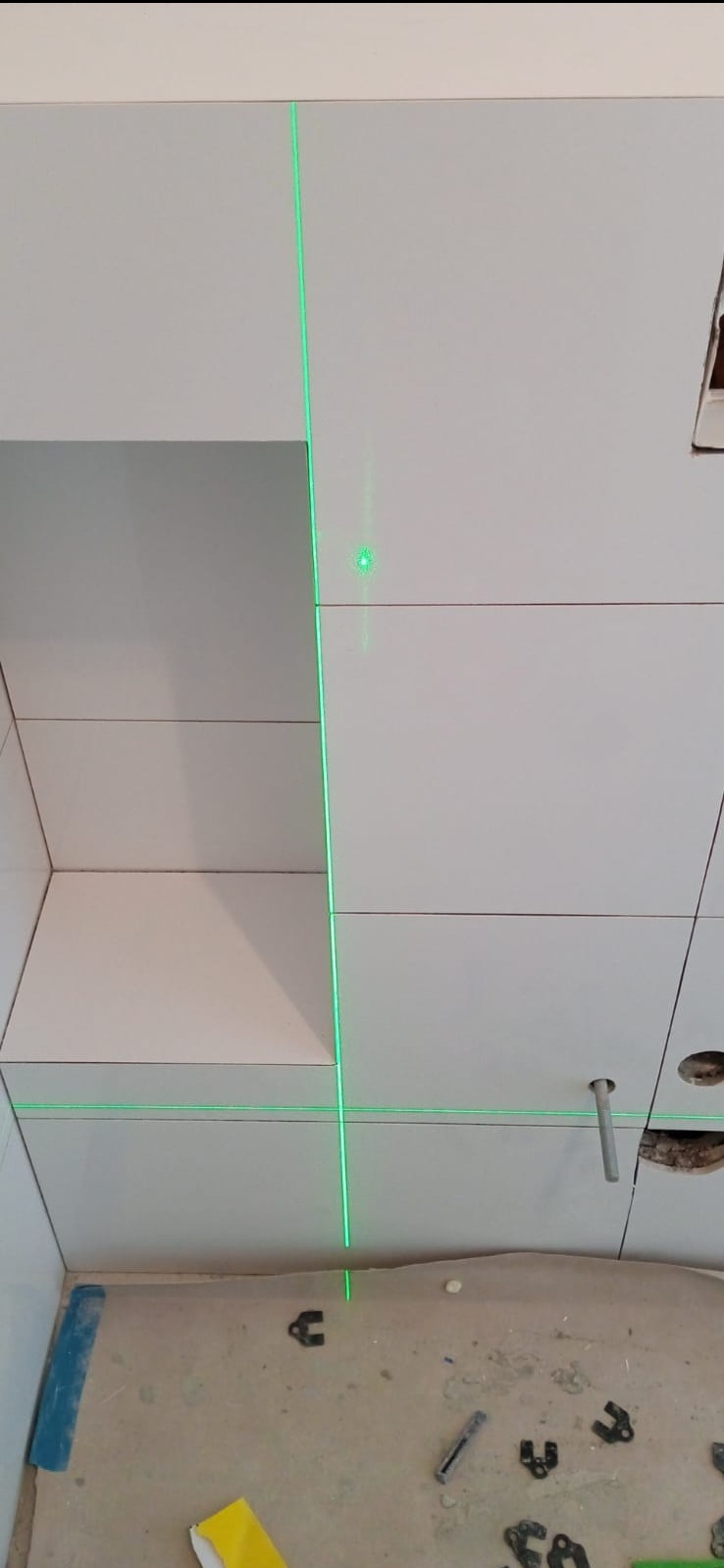 Białe płytki ścienne w łazience, układane z użyciem lasera krzyżowego. Widoczne akcesoria glazurnicze na podłodze. Ujęcie z dołu, podkreślające precyzję.