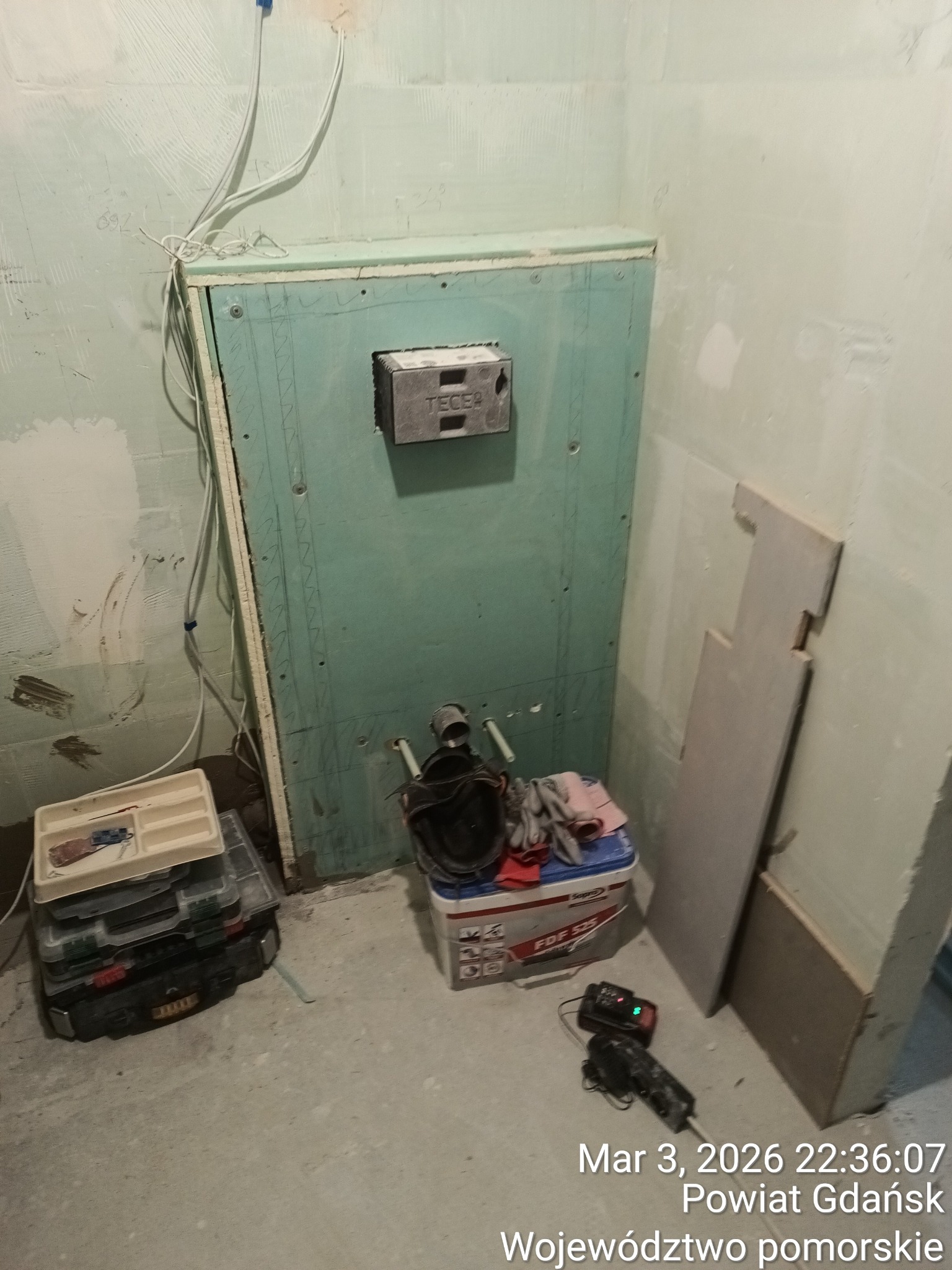 Stelaż podtynkowy TECE obudowany płytą GK w trakcie montażu w łazience. Widoczne narzędzia i materiały budowlane. Prace przygotowawcze przed wykończeniem.