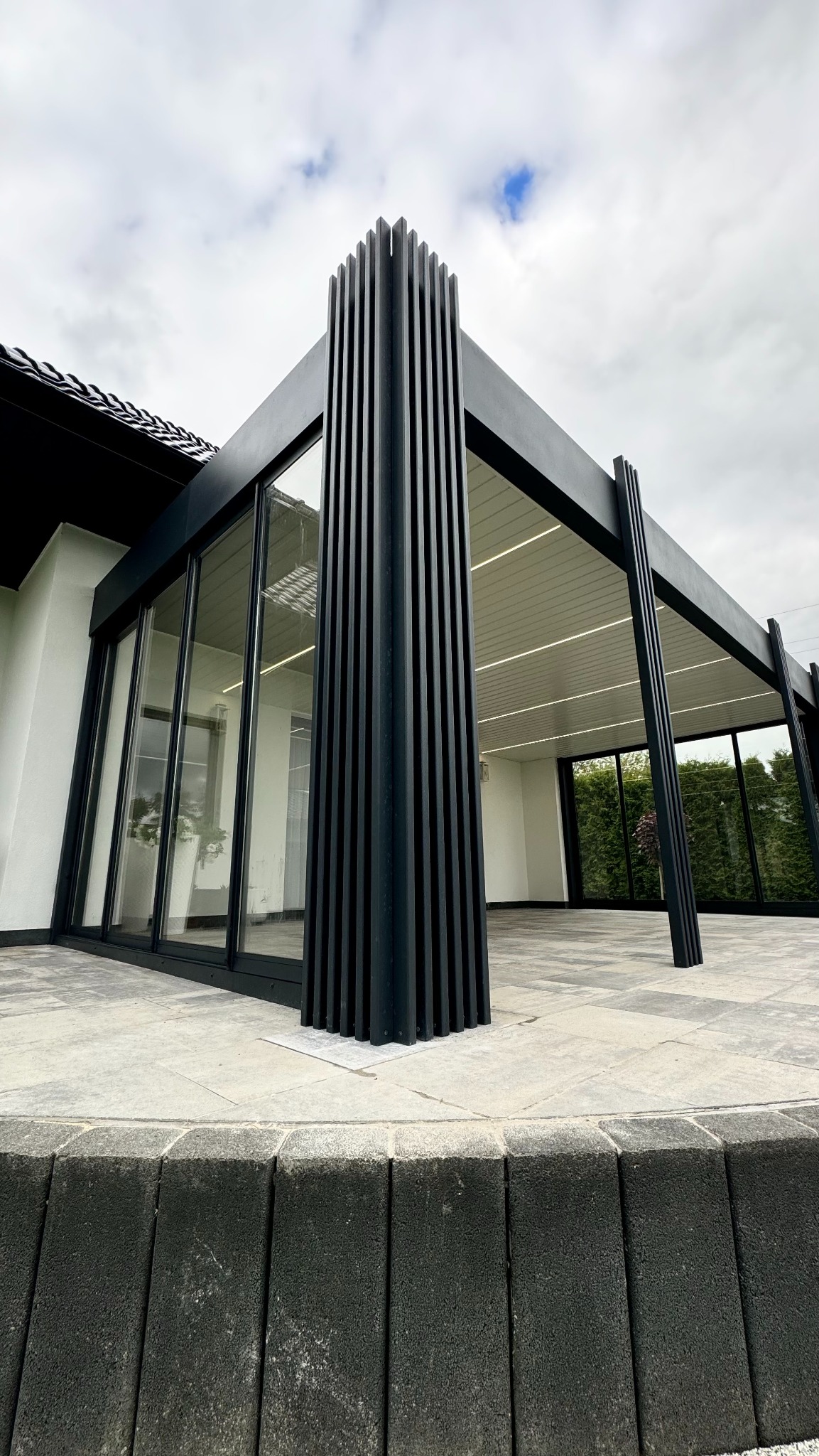 Nowoczesna pergola metalowa z pionowymi lamelami, przeszklonymi ścianami i oświetleniem LED, widziana z dołu, podkreślająca geometryczny design i minimalistyczny styl.