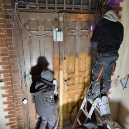 PAMAR PLUS SPÓŁKA Z OGRANICZONĄ ODPOWIEDZIALNOŚCIĄ - Renowacja drewnianych drzwi wejściowych metodą laserową. Dwóch pracowników usuwa starą farbę, stojąc na drabinie. Widoczny efekt czyszczenia laserem.