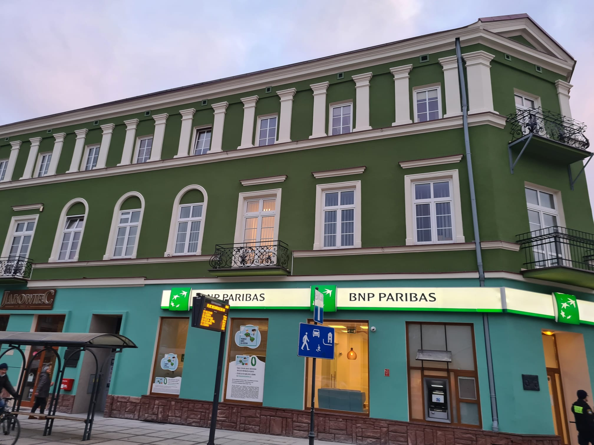 Odnowiona elewacja dwukondygnacyjnego budynku banku BNP Paribas w odcieniach zieleni i turkusu, z białymi kolumnami i balkonami, widok z poziomu ulicy.