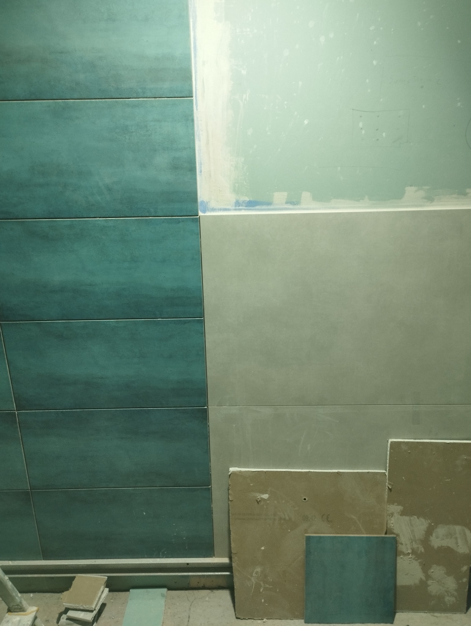 Fragment ściany w trakcie prac wykończeniowych: położone turkusowe płytki ceramiczne sąsiadują z surową płytą kartonowo-gipsową, na podłodze leżą resztki materiałów.