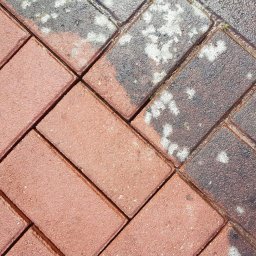 SEDONA AUTO MARCIN POKORSKI - Częściowo wyczyszczona, czerwona kostka brukowa ułożona w jodełkę. Po prawej stronie widoczne zabrudzenia, po lewej czysta powierzchnia. Widoczny logotyp firmy w lewym dolnym rogu.