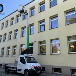 SEDONA AUTO MARCIN POKORSKI - Żółta elewacja budynku z wieloma oknami, czyszczona z podnośnika koszowego na białym samochodzie dostawczym. Widoczne odbicia drzew w szybach okien.