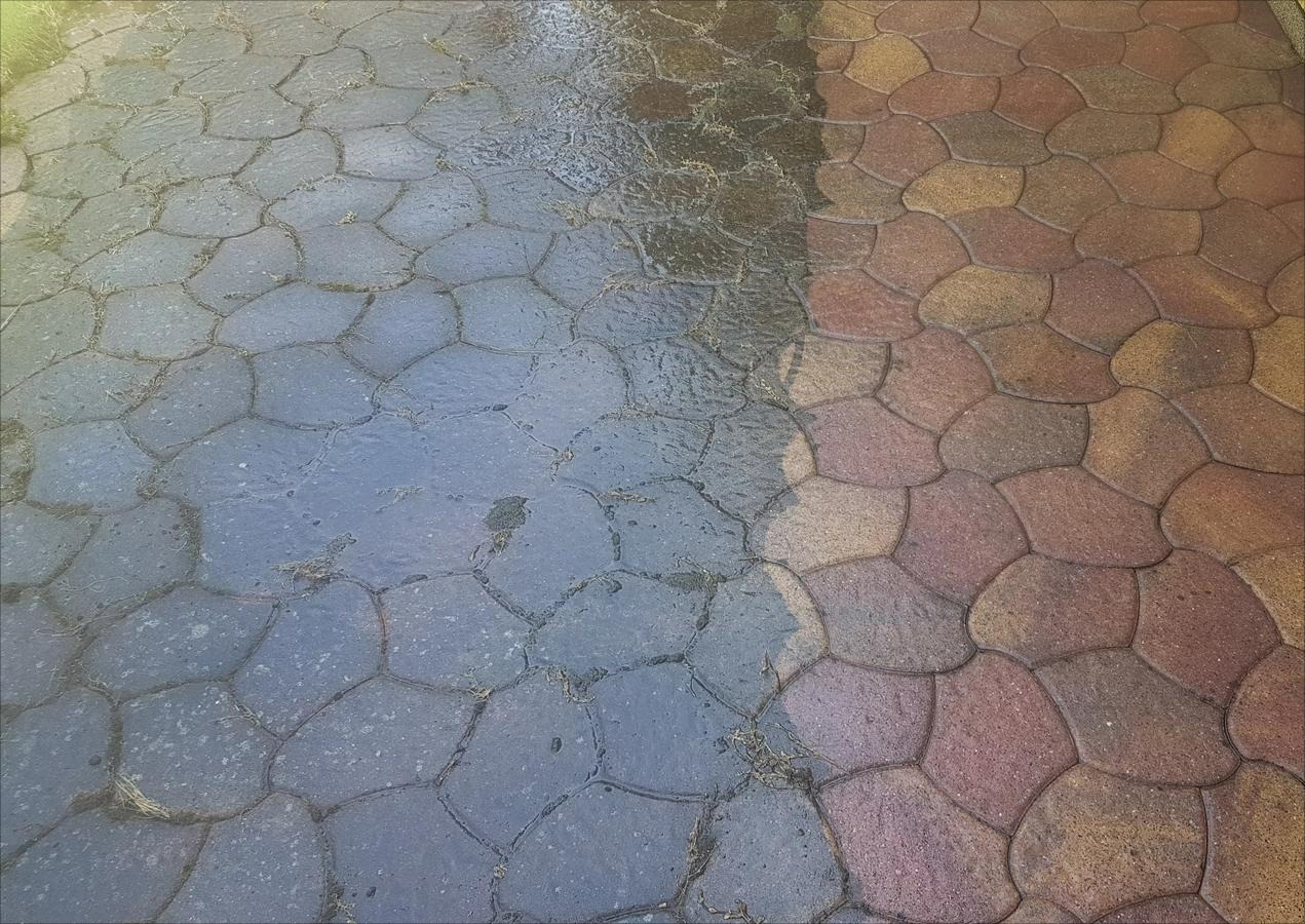 Kostka brukowa częściowo umyta, widoczna różnica w kolorze i czystości. Po lewej mokra, ciemna, po prawej sucha, w odcieniach brązu i czerwieni.