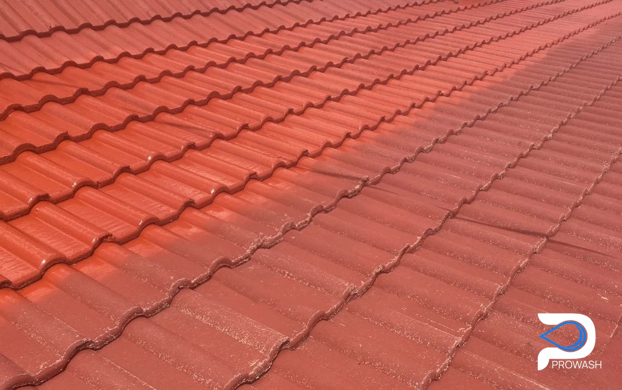 Czerwona dachówka ceramiczna, częściowo umyta, ukazująca różnicę w kolorze i czystości. Widoczny kontrast między czystą a zabrudzoną powierzchnią dachu.