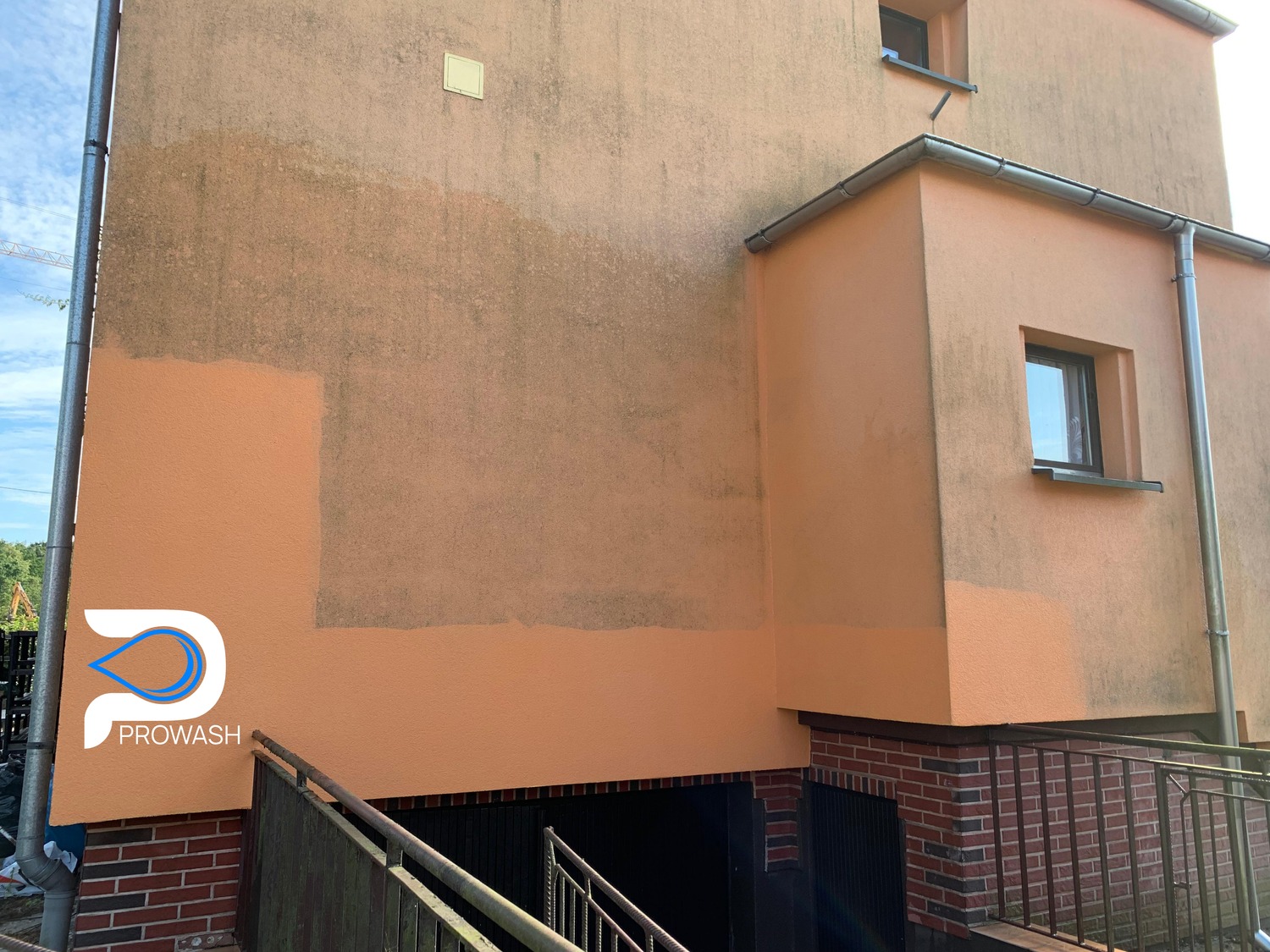 Częściowo umyta elewacja budynku w kolorze brzoskwiniowym, widoczne różnice w czystości. W lewym dolnym rogu logo firmy PROWASH.