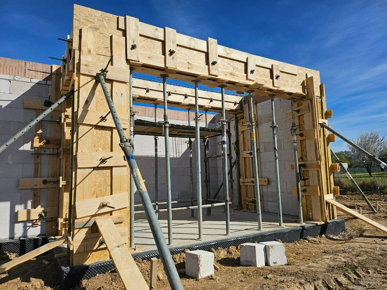 Szczegółowe ujęcie szalunku z desek i podpór stalowych, przygotowanego do wylania betonu na fundamencie budynku z bloczków, w słoneczny dzień.