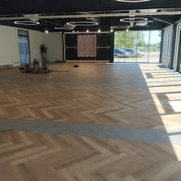 KING-FLOOR MIKOŁAJ CHMIEL - Układanie parkietu w jodełkę w przestronnym, nowoczesnym wnętrzu z oświetleniem LED. Widoczny fragment posadzki i narzędzia pracy.