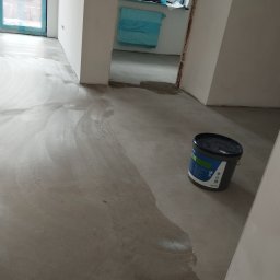 KING-FLOOR MIKOŁAJ CHMIEL - Wylewka samopoziomująca na podłodze w trakcie prac. Widoczne ślady rozprowadzania masy i wiadro z produktem. Przygotowanie podłoża pod panele lub wykładzinę.