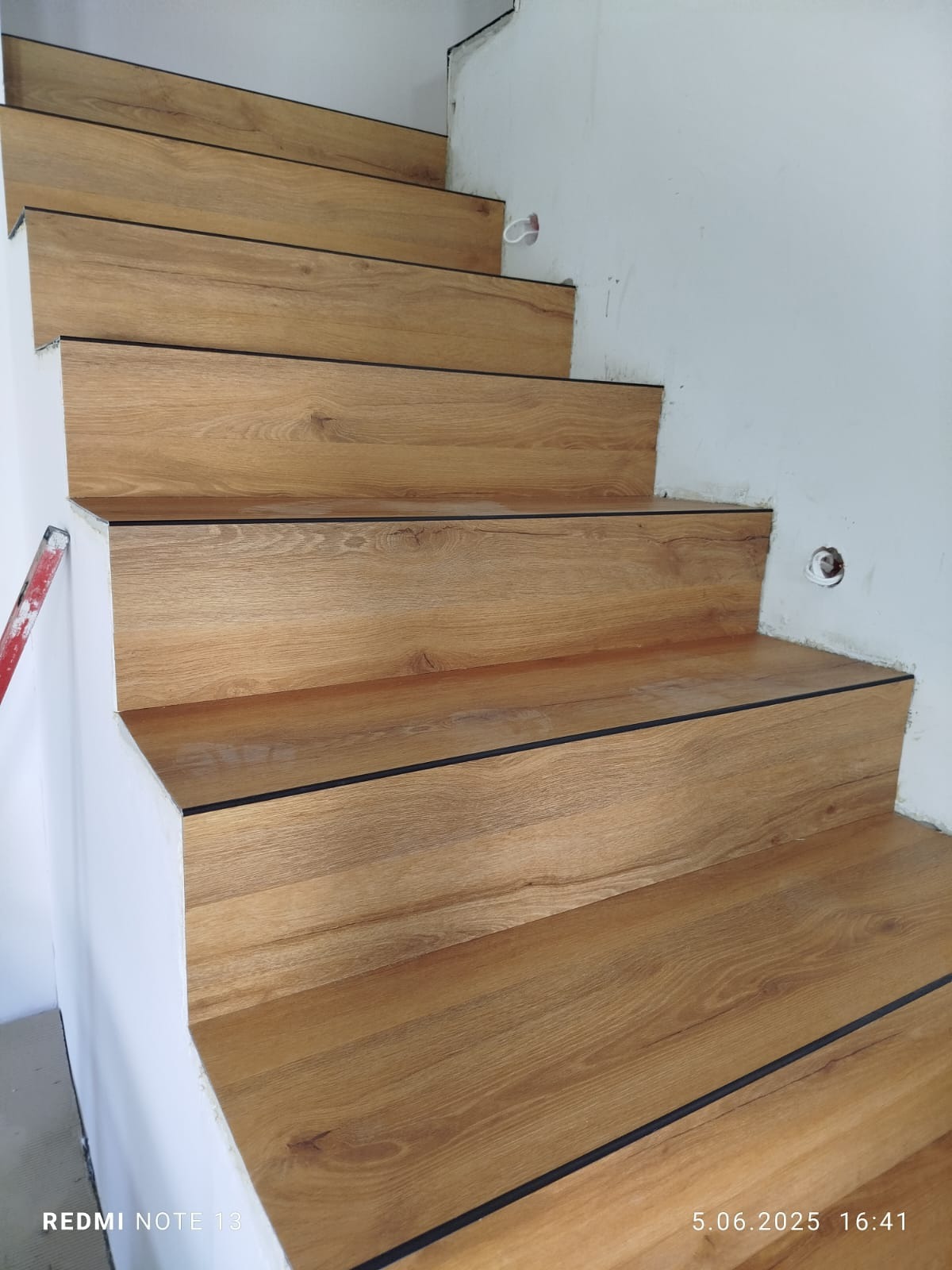 Schody wykończone panelami imitującymi drewno, z czarnymi listwami krawędziowymi, widok z dołu, częściowo wykończone ściany.