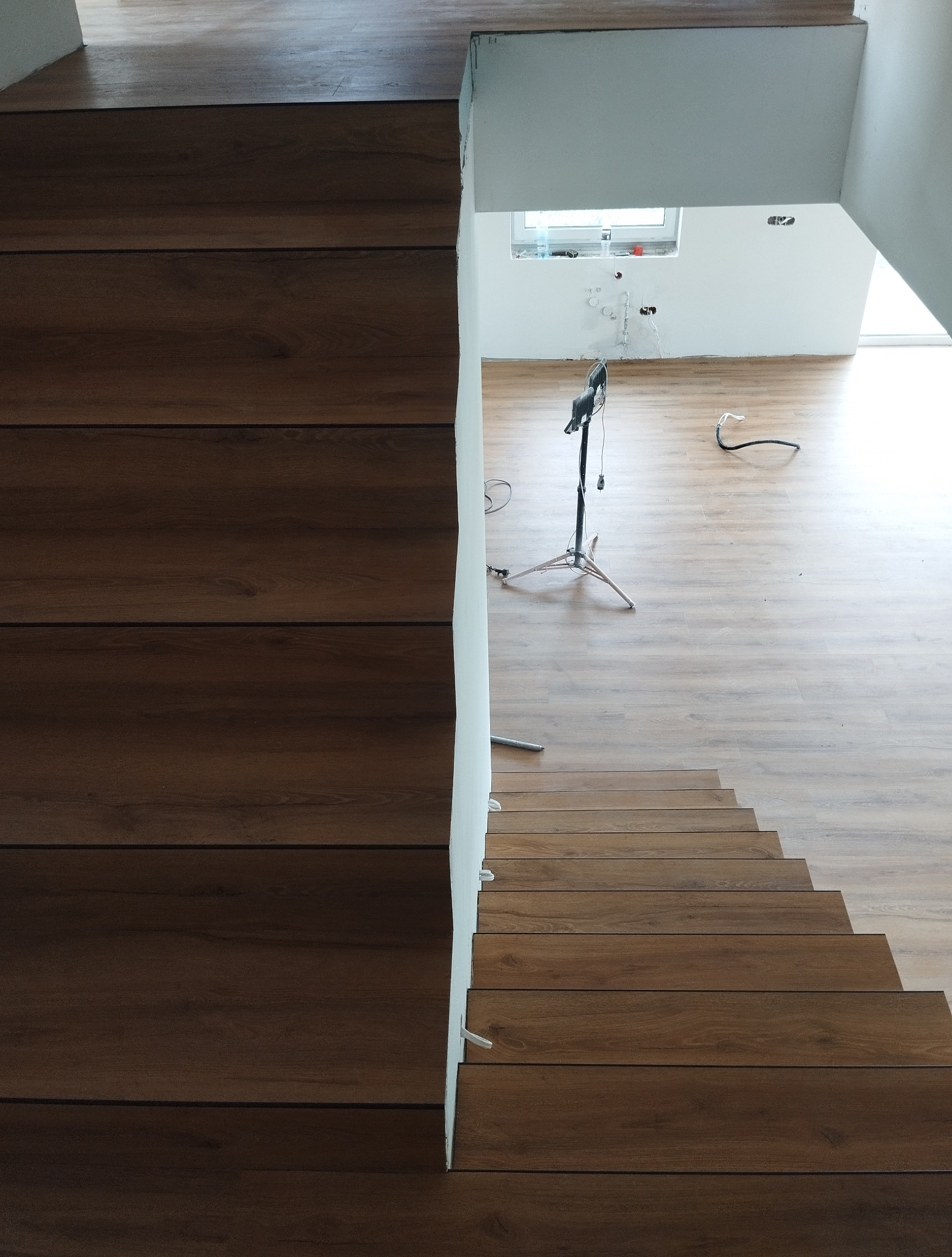 Ukończone schody z paneli drewnopodobnych, widok z góry. Na podłodze widoczny statyw oświetleniowy i przewody. Świeżo wykończone wnętrze.