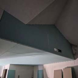 PROWORK - Montaż płyt karton-gips na skośnym suficie poddasza, widoczne płyty i konstrukcja, surowy stan wykończenia, przygotowanie do dalszych prac.
