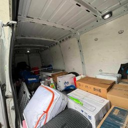 Clearbox - Wnętrze białego busa wypełnione kartonami i różnymi przedmiotami, gotowe do transportu. Widoczne pudełka IKEA i inne pakunki.