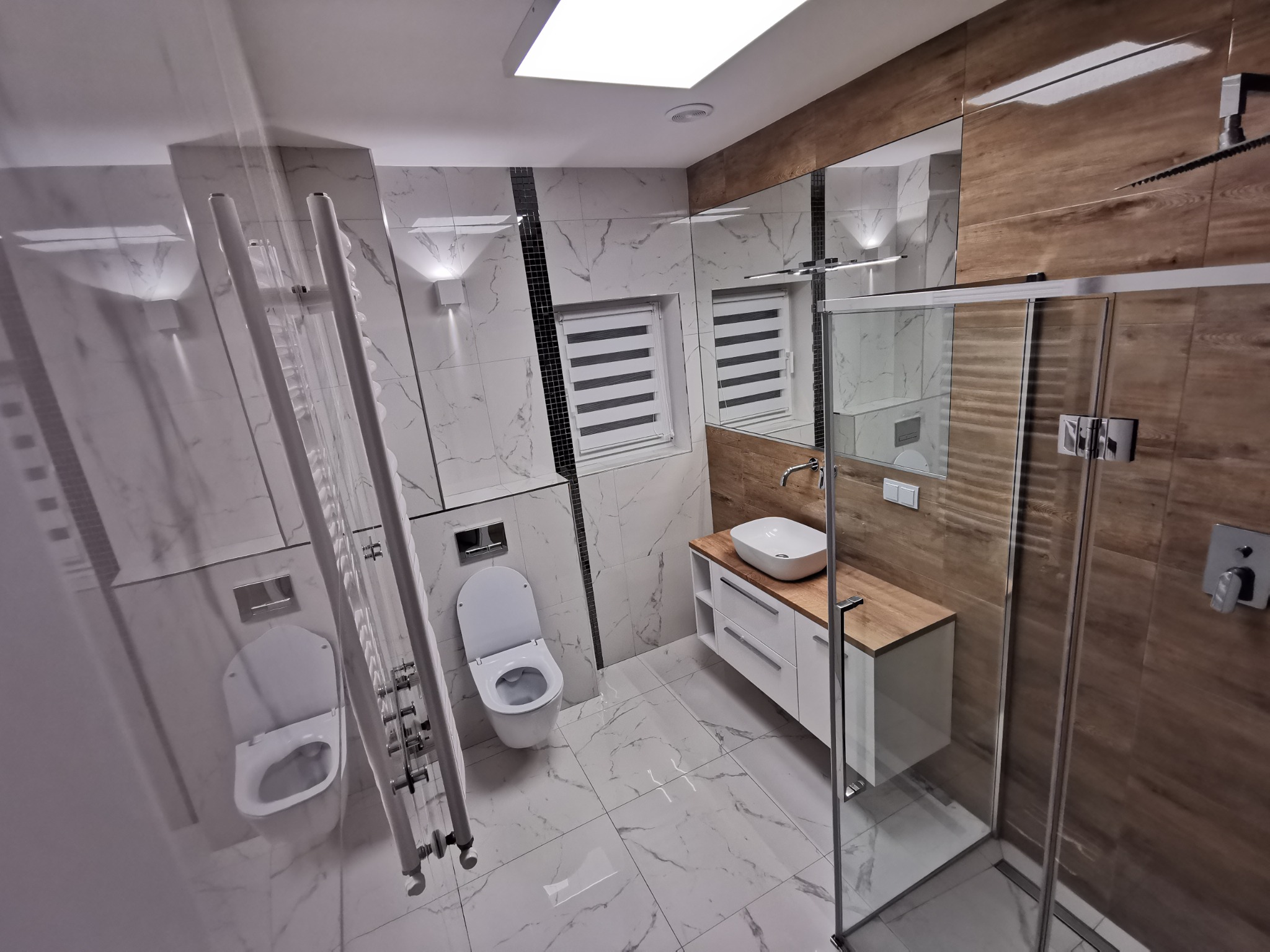 Nowoczesna łazienka z marmurowymi płytkami, drewnianymi akcentami i szklaną kabiną prysznicową. Grzejnik drabinkowy i podświetlane lustro dodają elegancji.