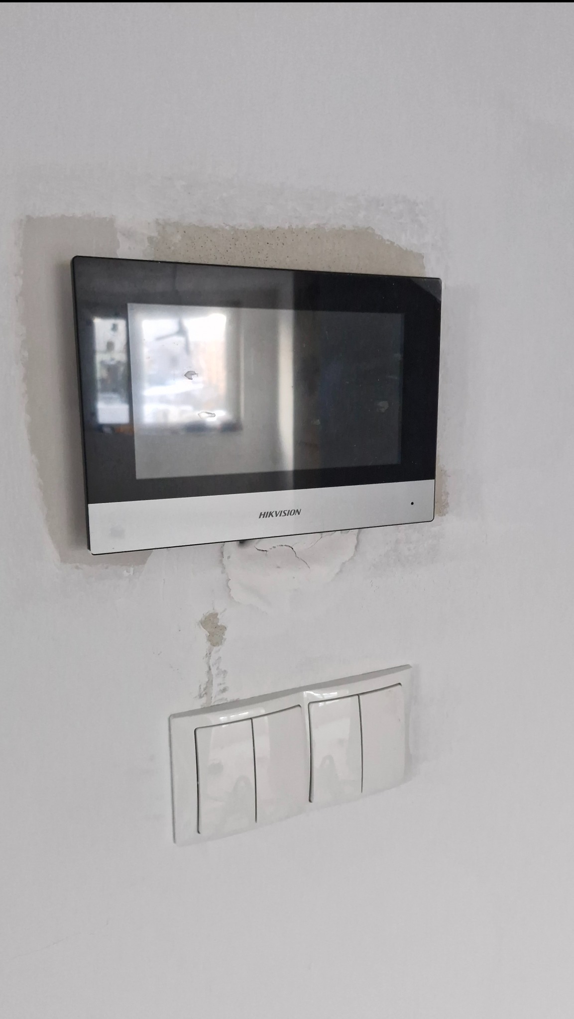 Zamontowany wideodomofon Hikvision na białej ścianie, poniżej włącznik światła. Widoczne ślady po montażu na ścianie.
