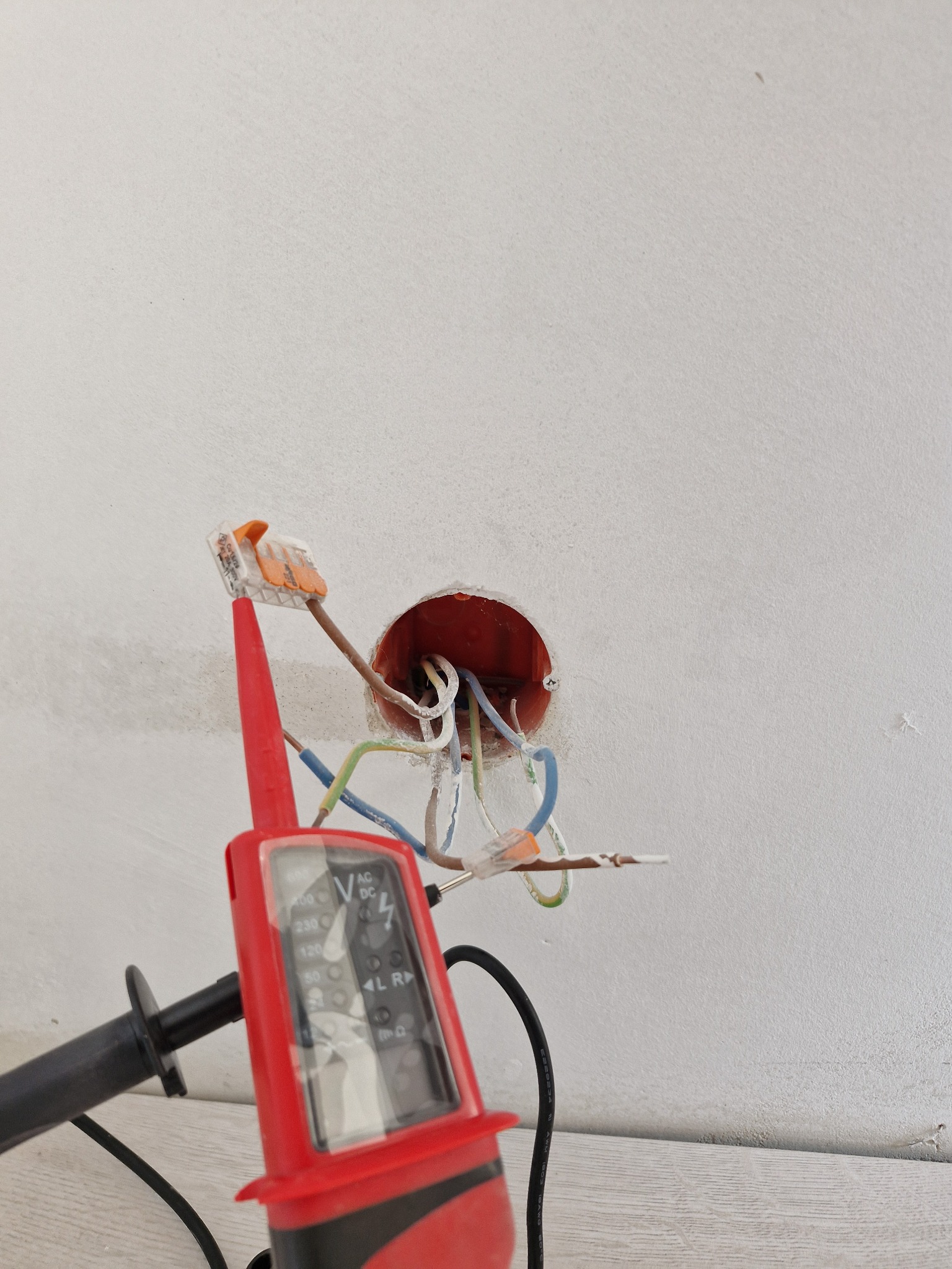 Przewody elektryczne w puszce podtynkowej, połączone złączkami WAGO, sprawdzane próbnikiem napięcia. Widoczne kolory izolacji przewodów.