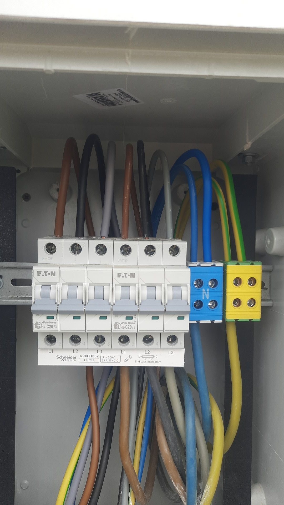 Rozdzielnica elektryczna z zamontowanymi bezpiecznikami Eaton i Schneider, widoczne kolorowe przewody i listwy zaciskowe wewnątrz skrzynki.