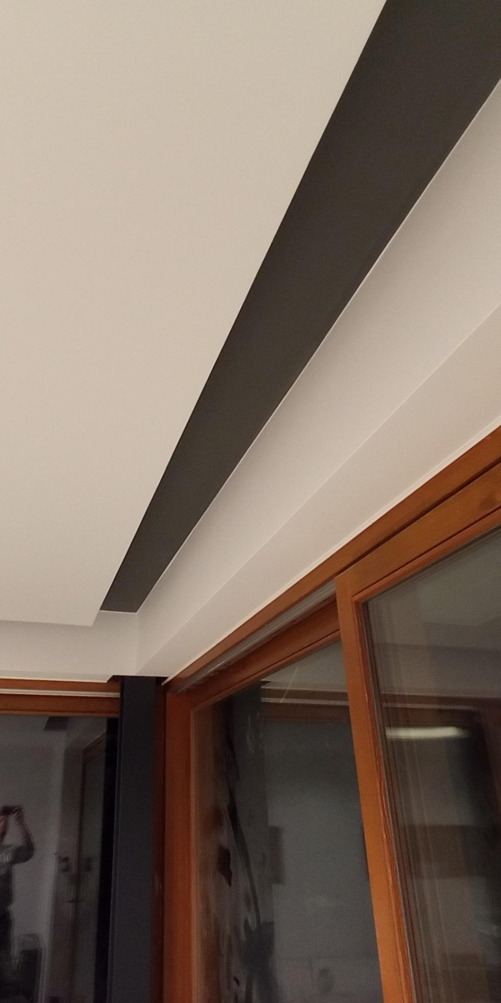 Pomysłowe wykończenie sufitu z ciemnym pasem i drewnianą stolarką okienną. Nowoczesny design wnętrza z dbałością o detale.