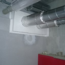 MIWO Jarosław Wojtach - Instalacja wentylacyjna z izolacją termiczną na suficie, widoczna czerwona szafka. Ujęcie z dołu, sufit z elementami instalacji.