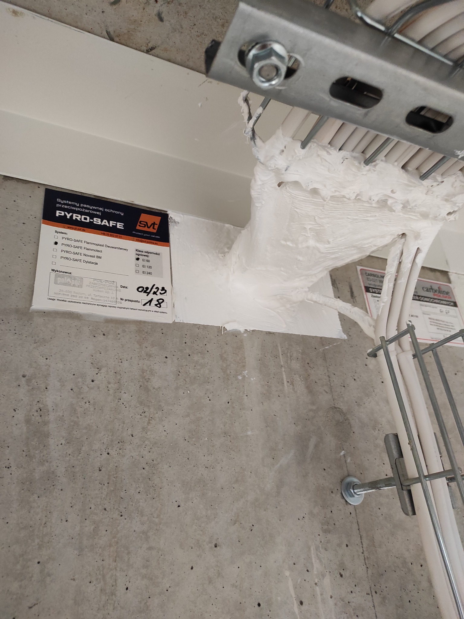 Zabezpieczenie przeciwpożarowe przepustów kablowych systemem Pyro-Safe w Pruszkowie. Widoczne kable uszczelnione białą masą i tabliczka informacyjna.
