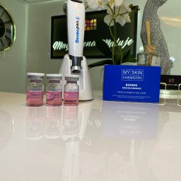 Marta Buchar COSMETOLOGY - DermaPen 4 z ampułkami Bioreg Skin Blemishes i pudełkiem My Skin Chemistry na błyszczącym blacie, w tle kwiaty i dekoracja pantery, sugerujące zabieg kosmetyczny.