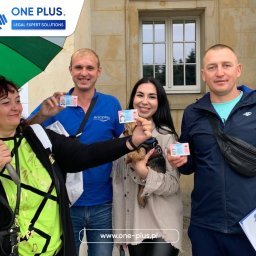 ONE PLUS Sp. z o.o. - Grupa osób we Wrocławiu trzyma dokumenty tożsamości, prawdopodobnie uzyskane dzięki wsparciu firmy. W tle budynek z oknem i kolorowy parasol.