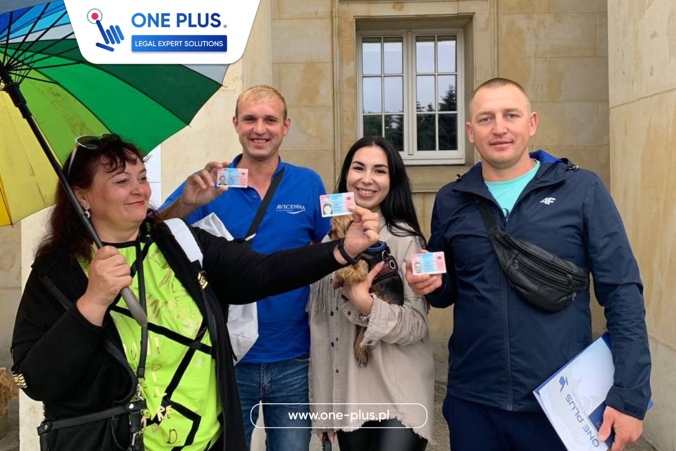 Grupa osób we Wrocławiu trzyma dokumenty tożsamości, prawdopodobnie uzyskane dzięki wsparciu firmy. W tle budynek z oknem i kolorowy parasol.